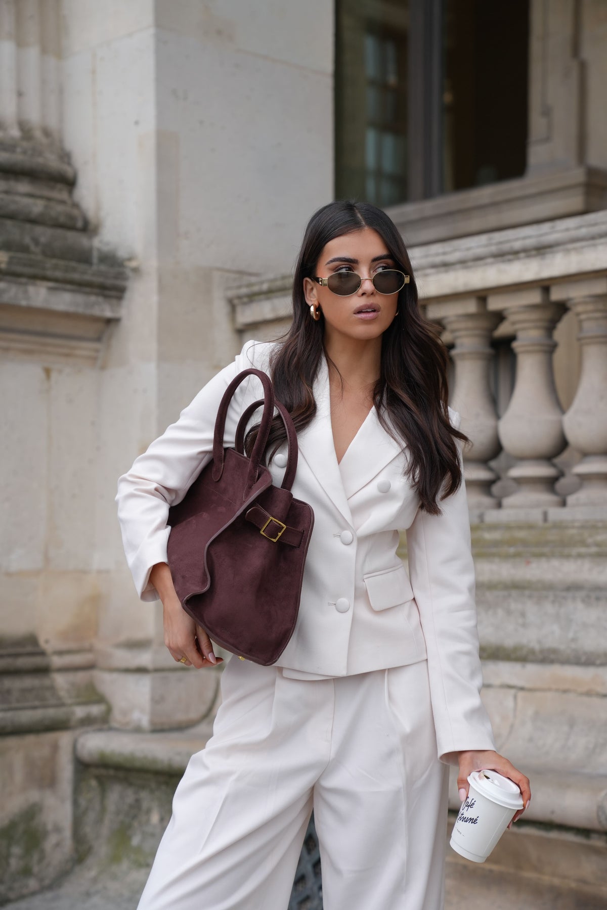 Woman in a cream blazer and wide-leg trousers carrying a burgundy handbag